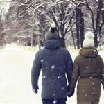 Two people in winter clothes hold hands and walk away down a snowy lane